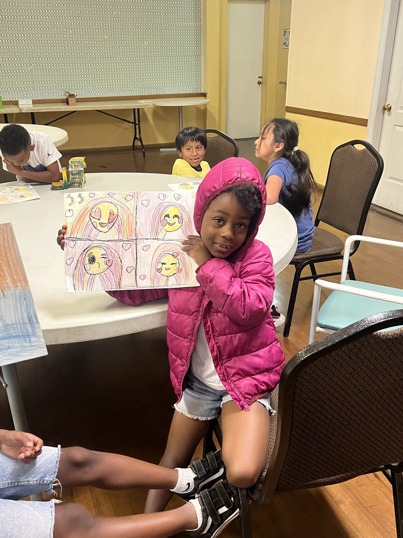 A student smiling and holding up her emoji drawings